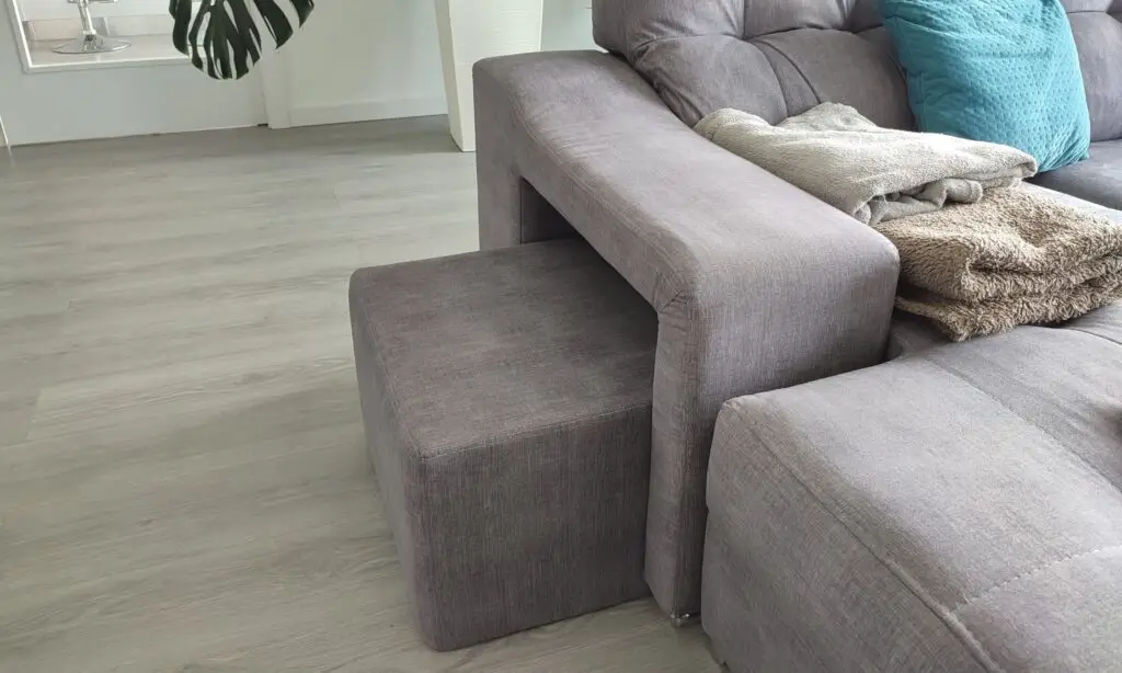 Pufe quadrado junto a um sofá cinzento escuro - tem o objetivo de servir como degrau para melhorar a mobilidade do cão idoso dentro de casa