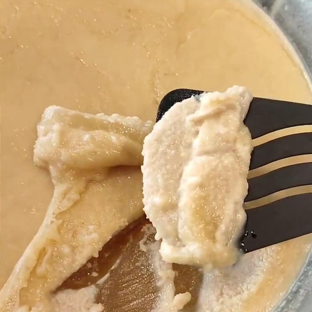 imagem de um caldo de ossos com textura gelatinosa num recipiente de vidro, com uma espátula a retirar o excesso de gordura que se acumulou na superfície