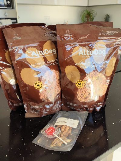 Embalagens de alimento desidratado da marca Altudog em cima de uma bancada e uma embalagem de snacks naturais da mesma marca.