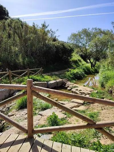Ponte de madeira com pequeno rio com alguma água, pedras e vegetação