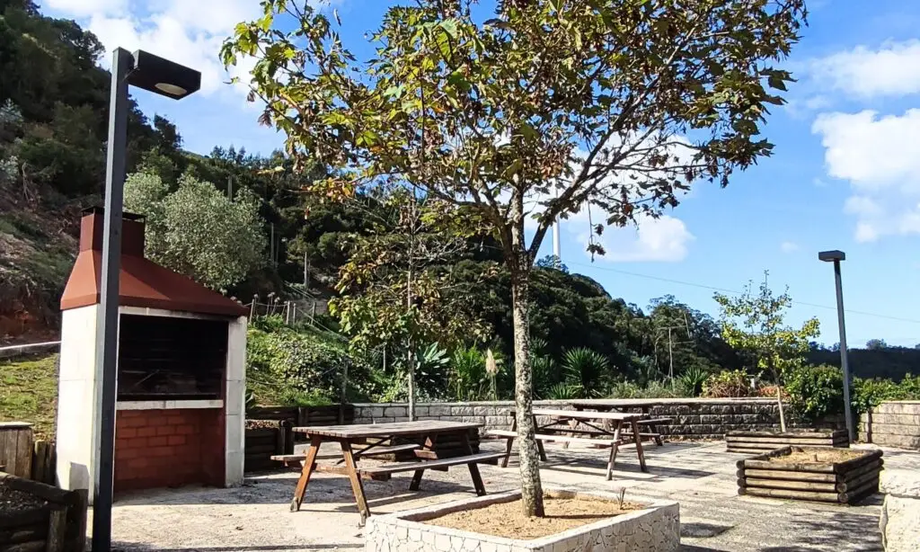 Parque de merendas com mesas e cadeiras, árvores e uma churrasqueira