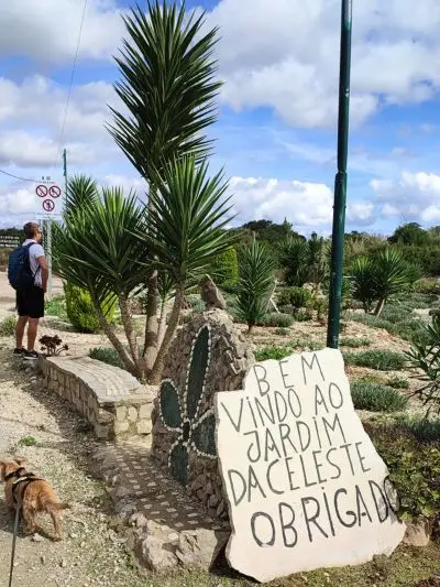 Homem com cão pequeno a observar paisagem. Ha uma placa de pedra no chão que diz: Bem-vindo ao jardim da celeste. Obrigado.