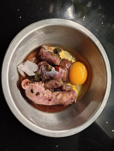 Taça com alimentação BARF para cães, composta por pescoço, moelas, coração e fígado de frango, ovo cru e a sua membrana, legumes, além de suplemento de vitamina D e ómega 3.