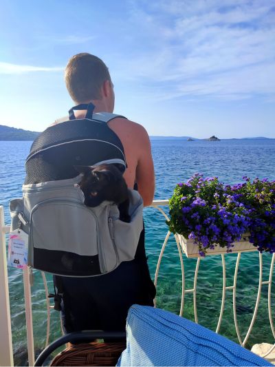 Homem a observar o mar com um gato paraplégico numa mochila para transporte de caes e gatos, no Amadria Park Camping Trogir