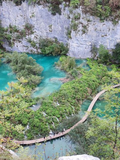 Pessoas a caminhar num passadiço em madeira com vegetação e água à volta, lagos de plitvice Croácia